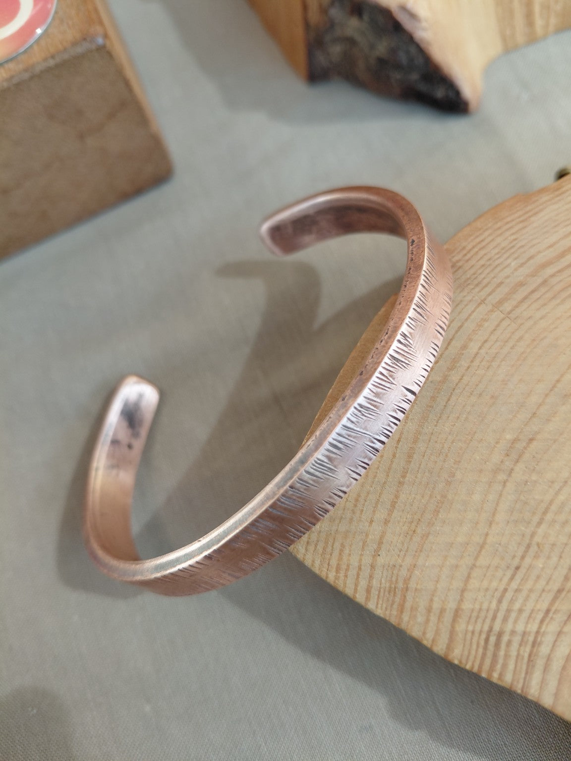 Textured copper cuff bracelet resting on wood