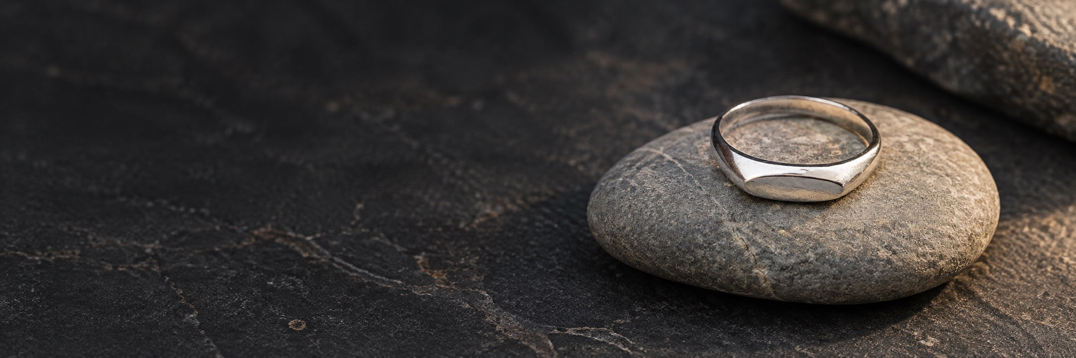 AI-generated editorial of a narrow oval silver signet ring on dark natural stone
